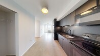 Located in the Analog building in downtown Tacoma, WA, Unit #202 is a thoughtfully designed second-floor residence that blends modern industrial aesthetics with clean, minimalist finishes. The layout flows efficiently across a single level, encompassing eight distinct spaces that make excellent use of the available square footage.

The galley-style kitchen is a standout feature, finished with dark matte cabinetry that extends to the ceiling, a black undermount sink with a matte black faucet, dark countertops, and under-cabinet lighting — creating a striking contrast against the bright, white walls. Light wood-tone flooring in the kitchen and living areas transitions seamlessly toward the main living space, which is bathed in natural light from large windows overlooking the Tacoma cityscape.

The bedroom areas feature polished concrete floors and generous windows that frame views of the surrounding urban neighborhood, filling the rooms with daylight. A dedicated walk-in closet provides ample storage with built-in shelving and hanging rods. The bathroom is finished with crisp white wall surrounds, a soaking tub, and matte black hardware and fixtures that echo the kitchen's contemporary style. Throughout the unit, the clean white walls and minimalist design create a bright, airy atmosphere well-suited to modern urban living.