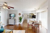 Located at 17200 NW 64th Ave in Hialeah, FL, this well-appointed one-bedroom, one-bathroom residence offers a thoughtfully designed single-floor layout that maximizes both comfort and functionality. Rich wood-style flooring flows throughout the main living areas, complemented by textured ceilings and a bright, neutral color palette.

The open-concept living and dining area is bathed in natural light from large sliding glass doors that lead to a private balcony, offering outdoor views of the surrounding landscape. A ceiling fan overhead enhances airflow, while sheer white curtains with gold-toned hardware add an elegant touch. The living room provides generous space for relaxing and entertaining.

The dining area features a pendant light fixture and connects seamlessly to the kitchen, which is equipped with dark espresso cabinetry, light quartz-style countertops, stainless steel appliances including a refrigerator, range, and microwave, and a functional breakfast bar.

A hallway with decorative wall accents leads to the spacious bedroom, which features plush carpeting, a ceiling fan, a natural-light window, and two closets for ample storage. The full bathroom includes a dark wood vanity with a framed mirror, white countertop, and a shower-tub combination.