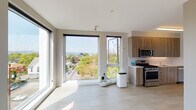 Located along NE Martin Luther King Jr Blvd in Portland's vibrant northeast corridor, this single-floor unit features a contemporary design characterized by clean lines, neutral tones, and an abundance of natural light. The open living and kitchen area is anchored by expansive floor-to-ceiling windows that frame elevated views of the surrounding neighborhood, treetops, and the broader Portland skyline. Light-toned tile flooring runs throughout the main living space, enhancing the bright and airy atmosphere.

The kitchen is well-appointed with warm wood-grain cabinetry extending to the ceiling, light quartz countertops, a white tile backsplash, and a full suite of stainless steel appliances including a gas range, microwave, dishwasher, and refrigerator. The layout provides efficient counter and storage space.

The bedroom is accessed via a sliding barn-style door and benefits from its own large windows offering additional outdoor views and natural light. Wood-toned flooring adds warmth to the space.

The bathroom features a soaking tub, a wood-grain vanity with a white countertop, and a large mirror with overhead lighting. An in-unit stacked washer and dryer provides added convenience. Overall, the space presents a modern, functional aesthetic suited to urban living.
