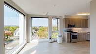 Located along NE Martin Luther King Jr Blvd in Portland's vibrant northeast corridor, this single-floor unit features a contemporary design characterized by clean lines, neutral tones, and an abundance of natural light. The open living and kitchen area is anchored by expansive floor-to-ceiling windows that frame elevated views of the surrounding neighborhood, treetops, and the broader Portland skyline. Light-toned tile flooring runs throughout the main living space, enhancing the bright and airy atmosphere.

The kitchen is well-appointed with warm wood-grain cabinetry extending to the ceiling, light quartz countertops, a white tile backsplash, and a full suite of stainless steel appliances including a gas range, microwave, dishwasher, and refrigerator. The layout provides efficient counter and storage space.

The bedroom is accessed via a sliding barn-style door and benefits from its own large windows offering additional outdoor views and natural light. Wood-toned flooring adds warmth to the space.

The bathroom features a soaking tub, a wood-grain vanity with a white countertop, and a large mirror with overhead lighting. An in-unit stacked washer and dryer provides added convenience. Overall, the space presents a modern, functional aesthetic suited to urban living.