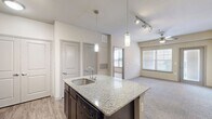 This thoughtfully designed one-bedroom, one-bathroom residence in Homestead offers a functional and comfortable single-floor layout. The open-concept kitchen and living area serves as the heart of the home, where wood-look flooring flows through the kitchen and transitions to plush carpet in the living room. The kitchen is equipped with rich dark wood cabinetry, granite countertops, a central island with a built-in sink and pendant lighting overhead, and black appliances including a refrigerator, range, and microwave. Track lighting and a ceiling fan provide ample illumination throughout the shared living space, which receives natural light from a large window. The bedroom is a comfortable retreat featuring soft carpeting, a ceiling fan, and a window with blinds. It provides direct access to the full bathroom, which includes a dark wood vanity, a tub-shower combination with tile surround, wood-look flooring, and a walk-in closet with built-in shelving. Additional practical spaces include a laundry area, a utility room, multiple pantry spaces, and two closets, ensuring generous storage throughout. The overall ambiance is clean, modern, and move-in ready.