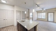 This thoughtfully designed one-bedroom, one-bathroom residence in Homestead offers a functional and comfortable single-floor layout. The open-concept kitchen and living area serves as the heart of the home, where wood-look flooring flows through the kitchen and transitions to plush carpet in the living room. The kitchen is equipped with rich dark wood cabinetry, granite countertops, a central island with a built-in sink and pendant lighting overhead, and black appliances including a refrigerator, range, and microwave. Track lighting and a ceiling fan provide ample illumination throughout the shared living space, which receives natural light from a large window. The bedroom is a comfortable retreat featuring soft carpeting, a ceiling fan, and a window with blinds. It provides direct access to the full bathroom, which includes a dark wood vanity, a tub-shower combination with tile surround, wood-look flooring, and a walk-in closet with built-in shelving. Additional practical spaces include a laundry area, a utility room, multiple pantry spaces, and two closets, ensuring generous storage throughout. The overall ambiance is clean, modern, and move-in ready.