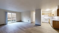 This single-floor residence offers a clean, functional layout with a neutral color palette and a variety of flooring finishes that distinguish the living spaces from the bedrooms. The open living and dining area is finished with light wood-look vinyl plank flooring and features a sliding glass door that leads to a private patio, allowing natural light to fill the space and providing outdoor views of a fenced yard. A structural column partially separates the living area from the kitchen, lending subtle definition to each zone.

The galley-style kitchen is efficiently designed with an abundance of light wood cabinetry extending to the ceiling, providing generous storage. White appliances—including a refrigerator, electric range, and dishwasher—are complemented by gray laminate countertops and a single-basin sink. Light tile-look flooring completes the kitchen's practical aesthetic.

The bedrooms are carpeted in neutral tones and receive natural light through standard windows with outdoor views of surrounding greenery and fencing. Each room offers a comfortable sense of space and includes closet access. The entry area features wood-look flooring and an adjacent closet, creating a welcoming transition into the unit. Overall, the space presents a straightforward, well-maintained interior suitable for everyday living.
