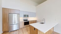 Located at 3405 SE Reed Dr. in Hillsboro, Oregon, this thoughtfully designed 3-bedroom, 2-bathroom single-floor residence offers a clean, contemporary aesthetic throughout. The open-concept living and kitchen area immediately impresses with dramatically vaulted ceilings that amplify the sense of space and an abundance of recessed lighting. A wall-mounted mini-split system provides efficient climate control.

The modern kitchen is a standout feature, equipped with stainless steel appliances including a French door refrigerator, electric range, and built-in microwave. Two-toned cabinetry — warm wood lower cabinets paired with light gray upper cabinets — extends to ceiling height, maximizing storage. A peninsula with a crisp white countertop and undermount sink adds functional workspace and casual seating potential. Light hardwood-style flooring unifies the main living areas.

The bedrooms feature soft carpeting and large floor-to-ceiling windows with bold black frames, flooding the rooms with natural light and offering views of the surrounding neighborhood's green landscaping. The primary bedroom provides a comfortable and well-proportioned retreat.

Both bathrooms are finished with warm wood vanities and hardwood-style flooring. One bathroom features an accessible layout with safety grab bars, while the second offers a full tub-shower combination with built-in cabinetry. A dedicated closet and in-unit laundry area complete this well-appointed residence.