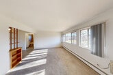 Located at 1099 Maiden Ln in Ann Arbor, Michigan, this one-bedroom, one-bathroom unit offers a practical and well-organized single-floor layout. The spacious living room is a highlight of the space, featuring a large bank of windows along one wall that flood the room with natural light and offer pleasant outdoor views of the surrounding neighborhood. Neutral carpet flooring and baseboard heating run throughout the main living areas, contributing to a clean and functional aesthetic.

The bedroom is a comfortable, well-proportioned room equipped with a ceiling fan, multiple windows with vertical blinds, and baseboard heating — providing both ventilation and views. Three closets are distributed throughout the unit, offering ample storage for residents.

The kitchen features warm-toned wooden cabinetry, a double sink, and white appliances including a refrigerator. It connects to a combined dining area, making efficient use of the available space. The flooring here transitions to a tile-style surface, practical for a kitchen setting.

The full bathroom includes a white vanity with sink, tiled tub-shower combination, a toilet, and a window for natural light and ventilation. A hallway connects the various rooms, creating a logical and easy-to-navigate flow throughout the unit.