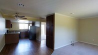 This single-story space showcases an open-concept layout that seamlessly connects the living area and kitchen, creating a cohesive and functional flow. The kitchen is equipped with dark espresso-toned cabinetry, including a tall floor-to-ceiling pantry cabinet that serves as a prominent architectural divider between the two spaces. A stainless steel refrigerator anchors the kitchen, which also features a sink positioned beneath a window, allowing natural light to illuminate the workspace. The cabinetry's rich, dark finish contrasts nicely with the light-colored walls throughout.

Crown molding runs along the ceiling perimeter, adding a refined detail to the interior. The flooring transitions between dark hardwood-style planks in the kitchen and living areas, providing a warm and durable surface underfoot. Ceiling-mounted HVAC vents and a ceiling fan ensure year-round climate comfort. Multiple windows allow natural light to filter into the space from various angles. The neutral wall tones and white baseboards create a clean, versatile backdrop suited to a variety of interior styles.