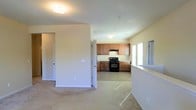 This single-floor residence offers a clean, functional layout designed for comfortable everyday living. The open floor plan allows the living area to flow naturally into the kitchen, creating a connected and easy-to-navigate space. The living area features neutral-toned carpeting that adds warmth underfoot, while crisp white walls and flush-mount ceiling lighting keep the interior bright and welcoming.

The kitchen is outfitted with warm medium-toned wood cabinetry that provides ample storage space across both upper and lower cabinets. Black appliances, including a gas range and an over-the-range ventilation unit, anchor the cooking area with a bold contrast against the lighter cabinetry and tile flooring. A window in the kitchen area allows natural light to filter in, enhancing the sense of openness throughout the space.

Interior doorways with white-paneled doors lead to additional rooms, suggesting a thoughtfully segmented floor plan that balances open communal areas with more private spaces. The neutral color palette throughout — from the beige carpet and tile to the white trim and walls — creates a cohesive, move-in-ready aesthetic. Overall, this single-level residence offers a practical and well-lit living environment suited to a variety of lifestyles.