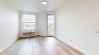 Located at 1245 N Anchor Way in Portland, OR, this well-appointed one-bedroom, one-bathroom unit offers a clean, modern aesthetic defined by light hardwood flooring and crisp white walls throughout. The open-concept kitchen serves as the centerpiece of the main living area, featuring sleek gray cabinetry, white quartz countertops, a central island with an undermount sink and matte black faucet, and a full suite of stainless steel appliances including a range, microwave, and refrigerator. Recessed lighting illuminates the kitchen and living area, which flows seamlessly toward a glass-panel balcony door, opening to a private outdoor space with open views of the surrounding Portland landscape. The bedroom is a comfortable, well-lit retreat with a large window framing city and waterway views, warm hardwood floors, and access to two closets — including a walk-in closet with wire shelving for ample storage. The full bathroom is finished with clean white surroundings, a soaking tub with a curved shower rod, and matte black fixtures for a contemporary touch. The overall ambiance is bright, airy, and move-in ready, with a consistent modern design language carried throughout the entire space.
