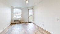 Located at 1245 N Anchor Way in Portland, OR, this well-appointed one-bedroom, one-bathroom unit offers a clean, modern aesthetic defined by light hardwood flooring and crisp white walls throughout. The open-concept kitchen serves as the centerpiece of the main living area, featuring sleek gray cabinetry, white quartz countertops, a central island with an undermount sink and matte black faucet, and a full suite of stainless steel appliances including a range, microwave, and refrigerator. Recessed lighting illuminates the kitchen and living area, which flows seamlessly toward a glass-panel balcony door, opening to a private outdoor space with open views of the surrounding Portland landscape. The bedroom is a comfortable, well-lit retreat with a large window framing city and waterway views, warm hardwood floors, and access to two closets — including a walk-in closet with wire shelving for ample storage. The full bathroom is finished with clean white surroundings, a soaking tub with a curved shower rod, and matte black fixtures for a contemporary touch. The overall ambiance is bright, airy, and move-in ready, with a consistent modern design language carried throughout the entire space.