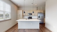 This single-floor residence showcases a clean, contemporary design throughout its well-appointed layout. The open-concept living and kitchen area serves as the heart of the home, where rich hardwood-style flooring flows seamlessly underfoot. The kitchen is a standout feature, equipped with light wood cabinetry, white quartz countertops, a classic subway tile backsplash, and a full suite of stainless steel appliances including a range, microwave, and French door refrigerator. A large central island with an integrated sink provides both additional workspace and a natural gathering point, illuminated by stylish pendant lighting above.

The bedroom offers plush carpeting and direct access to a spacious walk-in closet outfitted with wire shelving systems. The bathrooms maintain the home's modern aesthetic, featuring light wood vanities with quartz countertops, large-format tile flooring, and a tiled tub-shower combination. A dedicated laundry room houses a full-sized washer and dryer alongside overhead wire shelving for added storage convenience. Throughout, neutral tones, recessed lighting, and an abundance of natural light from well-placed windows create a bright, cohesive, and move-in-ready atmosphere.