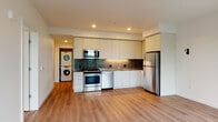 This contemporary single-floor residence showcases a clean, modern design with light-toned hardwood-style flooring that flows seamlessly throughout every room, creating a cohesive and inviting atmosphere.

The open-concept kitchen is a standout feature, outfitted with flat-front white cabinetry extending to the ceiling for ample storage, stainless steel appliances including a range, microwave, dishwasher, and refrigerator, and a striking dark tile backsplash that adds contrast and visual depth. The kitchen opens directly into a spacious living area bathed in natural light from large windows that frame lush green tree views, enhancing the sense of openness.

A dedicated alcove conveniently houses a stacked washer and dryer unit, offering in-unit laundry without sacrificing living space. The residence includes two full bathrooms, each finished with vertically stacked white subway tile in the tub-shower surround, dark countertop vanities with undermount sinks, large mirrors, and wood-look flooring for a polished, contemporary feel.

The bedroom features corner windows that invite abundant natural light and offer pleasant outdoor views, along with a sliding-door closet providing generous built-in storage. Recessed lighting throughout the unit ensures a well-lit environment, while the crisp white walls and minimal design aesthetic lend the space a fresh, modern character.
