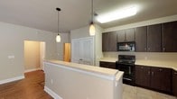 This single-floor residence offers a thoughtfully designed layout that balances functionality and comfort. The open-concept kitchen is a standout feature, showcasing rich dark espresso cabinetry with brushed silver hardware, light-toned countertops, and a full suite of black appliances including an electric range, over-the-range microwave, and refrigerator. Tile flooring runs throughout the kitchen, which flows naturally into the living area via a breakfast bar accented by stylish pendant lighting.

The living area is generously proportioned, featuring warm hardwood-style flooring, neutral-toned walls, a ceiling fan, and windows that allow natural light to fill the space. The open sightlines between the kitchen and living room create an inviting, connected atmosphere.

The two bedrooms are well-sized and carpeted, each with windows fitted with blinds and neutral wall tones that lend a calm, restful ambiance. One bedroom features a ceiling fan for added comfort.

The primary bathroom includes a dual-sink vanity with dark cabinetry, a large mirror, tile flooring, a separate tub and shower, and direct access to a walk-in closet with built-in shelving. The secondary bathroom mirrors the design aesthetic with a single-sink dark vanity, tile flooring, and a tub-shower combination. Together, these spaces offer a cohesive, move-in-ready living environment.