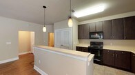 This single-floor residence offers a thoughtfully designed layout that balances functionality and comfort. The open-concept kitchen is a standout feature, showcasing rich dark espresso cabinetry with brushed silver hardware, light-toned countertops, and a full suite of black appliances including an electric range, over-the-range microwave, and refrigerator. Tile flooring runs throughout the kitchen, which flows naturally into the living area via a breakfast bar accented by stylish pendant lighting.

The living area is generously proportioned, featuring warm hardwood-style flooring, neutral-toned walls, a ceiling fan, and windows that allow natural light to fill the space. The open sightlines between the kitchen and living room create an inviting, connected atmosphere.

The two bedrooms are well-sized and carpeted, each with windows fitted with blinds and neutral wall tones that lend a calm, restful ambiance. One bedroom features a ceiling fan for added comfort.

The primary bathroom includes a dual-sink vanity with dark cabinetry, a large mirror, tile flooring, a separate tub and shower, and direct access to a walk-in closet with built-in shelving. The secondary bathroom mirrors the design aesthetic with a single-sink dark vanity, tile flooring, and a tub-shower combination. Together, these spaces offer a cohesive, move-in-ready living environment.