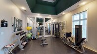 The fitness center at Resort At Lake Crossing is a thoughtfully designed, single-floor workout facility that combines functional equipment with an attractive interior aesthetic. The room's most distinctive architectural feature is its bold dark green tray ceiling, which adds visual depth and a resort-like character to the space. Ceiling fans are integrated into the tray ceiling, promoting air circulation throughout workouts.

Natural light enters through multiple windows fitted with white blinds, keeping the space bright and airy. Large floor-to-ceiling mirrors line one wall, visually expanding the room while allowing users to monitor their form during exercise. The durable rubber flooring provides cushioning and stability across the entire workout area.

The facility is well-stocked with a comprehensive range of equipment. Cardio options include treadmills, an elliptical, a stationary bike, and a rowing machine. Strength training is supported by a multi-functional cable machine, a weight bench, and a tiered dumbbell rack holding a full range of free weights. Additional accessories such as medicine balls, stability balls, and resistance bands are available for varied training routines. A wall-mounted television is positioned for easy viewing during cardio sessions. Decorative artwork on the walls and tasteful greenery contribute to the polished, welcoming ambiance of the space.