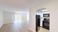 This single-floor residence offers a thoughtfully designed layout that balances open living spaces with private bedroom areas. The living room is a standout feature, characterized by light-toned hardwood-style flooring and a large window dressed with vertical blinds that allow ample natural light to fill the space. A graceful arched doorway connects the living area to the kitchen, creating an open yet defined flow between the two spaces.

The kitchen is efficiently laid out and well-equipped, featuring white cabinetry, granite-look countertops, and a full suite of black appliances including a refrigerator, range, over-the-range microwave, and dishwasher. A skylight overhead provides additional brightness, enhancing the clean, functional aesthetic of the space.

The bedrooms are carpeted and finished in neutral tones, offering a comfortable and quiet atmosphere. Each room includes closet storage—one featuring sliding double doors and another with a bifold door—along with windows fitted with vertical blinds for natural light and privacy. The overall design of the unit is clean and understated, with white trim, neutral walls, and consistent finishes throughout that create a cohesive and move-in ready environment.