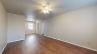 This single-floor residence offers a clean, functional layout designed for comfortable everyday living. The main living area is spacious and bright, featuring rich hardwood-style flooring that extends throughout the common spaces, neutral beige walls, and a textured ceiling with a ceiling fan and integrated light fixture. Natural light filters in through window blinds, enhancing the open feel of the room. A closet with a paneled door provides convenient built-in storage within the living area.

The bedroom continues the warm aesthetic with plush wall-to-wall carpeting, a ceiling fan, and a window that brings in soft natural light, creating a calm and restful atmosphere.

The kitchen is equipped with a white electric range, overhead cabinetry with an exhaust hood, light countertops, and a door with a window that allows additional natural light and outdoor access. The layout is compact yet practical for everyday meal preparation.

The bathroom features a white vanity with under-sink cabinetry, a solid surface countertop, a mirrored medicine cabinet above the sink, and chrome fixtures and hardware. The hardwood-style flooring continues into this space, tying the unit together cohesively.

Overall, this residence presents a tidy, well-maintained interior with consistent finishes and ample natural light throughout.