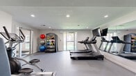 Located at 6006 E 126th St in Grandview, Missouri, this dedicated fitness center offers a well-appointed, single-floor workout facility designed to support a wide range of exercise routines. The space features clean white walls, recessed lighting, and a smooth, durable gray floor, creating a bright and functional environment for physical activity.

Cardio equipment is a highlight of the room, with multiple Spirit-brand treadmills and an elliptical machine positioned for comfortable use. A large flat-screen television mounted on a full-length wall mirror adds an entertainment element while maximizing the sense of space. The mirrored wall also benefits strength training, allowing users to monitor form during workouts.

The strength training area includes a multi-function cable machine and a dedicated rack of kettlebells, catering to both resistance and functional training. A separate freestanding rack houses an assortment of medicine balls and exercise balls in various sizes and weights, ideal for dynamic and core-focused workouts. A rowing machine rounds out the cardio offerings.

Natural light filters in through multiple windows and glass doors, one of which opens to an outdoor area, enhancing the overall ambiance of the space. The layout is open and thoughtfully organized, ensuring ease of movement between equipment zones. This fitness center provides a comprehensive and well-maintained environment suited for diverse training needs.