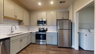 Located at 510 Morning Oak Drive in Westfield, Indiana, this single-floor home offers a clean, modern aesthetic throughout its thoughtfully designed layout. The kitchen is a standout feature, outfitted with gray shaker-style cabinetry, a classic white subway tile backsplash, light countertops, and a full suite of stainless steel appliances including a refrigerator, range, and over-the-range microwave. Rich hardwood-style flooring anchors the kitchen and extends into adjacent areas, creating a cohesive flow. The open living area transitions seamlessly from hard flooring to plush neutral carpeting, providing a comfortable and versatile space. Multiple carpeted bedrooms offer a quiet retreat, with at least one featuring vaulted ceilings that enhance the sense of openness, along with windows that allow natural light to fill the room. The primary bathroom is well-appointed with gray vanity cabinetry, white countertops, a soaking tub, and large-format tile surround, while a separate glass-enclosed walk-in shower adds a refined touch. A dedicated laundry room with a full-size washer and dryer provides added convenience. Neutral gray tones and white trim throughout the home create a cohesive, move-in-ready atmosphere.