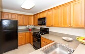 Located at 32 Blacks Ln in Springfield, NJ, this single-floor residence offers a thoughtfully laid-out living space with a neutral, warm color palette throughout. The open-concept layout, visible in the dollhouse view, connects the kitchen and living areas seamlessly. The kitchen is outfitted with warm wood cabinetry, ample counter space, and black appliances including a gas range with an over-the-range microwave, providing a functional and efficient cooking environment. The carpeted bedrooms are generously sized, each featuring large windows with blinds that frame lush, wooded views, allowing natural light to fill the rooms. The primary bedroom is notably spacious and includes dual closets with built-in shelving, offering excellent storage. The hallway area features multiple closets and an intercom system, adding convenience and security. Two full bathrooms are finished consistently, each featuring warm wood vanities with light countertops and large mirrors. One bathroom includes a walk-in glass-door shower stall, while the other is equipped with an accessibility grab bar. Soft, neutral wall tones and plush carpeting throughout contribute to a calm and comfortable ambiance, making this a welcoming residential space.