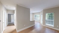 Located on McQueen Drive in Durham, NC, this single-floor, one-bedroom, one-bathroom residence offers a thoughtfully designed layout with modern finishes throughout. The galley-style kitchen is a standout feature, showcasing white shaker cabinetry, granite-look countertops, stainless steel appliances including a refrigerator, dishwasher, and range, as well as light hardwood-style flooring that carries through the main living areas. Large windows in the kitchen and living area allow ample natural light to fill the space, offering views of the surrounding greenery. The open living area features neutral gray walls, crown molding, and clean lines that create a bright and airy atmosphere. The bedroom is a comfortable retreat with plush carpeting, a ceiling fan, and a window with blinds for natural light and privacy. It connects to a generously sized walk-in closet fitted with wire shelving for organized storage. The full bathroom features a white vanity with granite-look counters, a large mirror with vanity lighting, and a tub-shower combination. A dedicated laundry area houses a full-size washer and includes a water heater, adding everyday convenience. This residence delivers a clean, functional, and contemporary living experience.