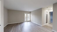 Located at 14505 Old Courthouse Way in Newport News, Virginia, this 2-bedroom, 1-bathroom residence offers a thoughtfully designed single-floor layout with clean, modern finishes throughout. The living room is bright and open, featuring light-toned laminate flooring, neutral taupe walls, and French doors that lead to a private balcony with outdoor views — an inviting space filled with natural light. Adjacent to the living area, the galley-style kitchen is efficiently designed with white cabinetry, granite-look countertops, a stainless steel double sink with a matte black faucet, and stainless steel appliances including a range and dishwasher, all set on matching light wood flooring. The spacious primary bedroom is carpeted for comfort and features a double-door closet with built-in shelving and direct access to the full bathroom. The second bedroom is similarly finished with plush carpet, a bright window with blinds, and generous closet space. The shared full bathroom is clean and contemporary, offering a white vanity, framed mirror, and matte black fixtures with a tub-shower combination. A connecting hallway ties all rooms together seamlessly, contributing to the home's efficient and comfortable flow throughout.