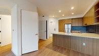 Located at 201 Del Sol Dr in San Diego, CA, this single-floor residence offers a clean, modern aesthetic throughout. The open-concept kitchen is a standout feature, showcasing warm wood cabinetry, a bold navy tile backsplash, stainless steel appliances including a gas range and refrigerator, and a generous island with a light quartz countertop and undermount sink — ideal for both cooking and casual dining. Recessed lighting illuminates the kitchen and living area, which flows seamlessly across light-toned hardwood flooring that extends throughout the unit. The bedroom features crisp white walls, the same warm wood flooring, and a large window with an outdoor balcony view that fills the room with natural light. A second room, accessible via a hallway with louvered closet doors, offers additional flexibility. The bathroom is appointed with a wood-grain vanity, light quartz countertop, undermount sink, a sleek modern faucet, and a backlit frameless mirror that adds a refined touch. The overall design is cohesive and contemporary, combining neutral tones, natural wood accents, and modern finishes to create a bright, functional, and inviting living environment.