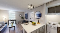 Located at 170 E Griffith St in the heart of Jackson, Mississippi, this single-floor residence offers a well-organized, open-concept layout with modern finishes throughout. The kitchen serves as a central hub, featuring gray shaker-style cabinetry, a white countertop island ideal for casual dining or meal prep, and track lighting overhead that provides focused, adjustable illumination. The kitchen flows seamlessly into the living and dining areas, creating an interconnected space well-suited for everyday living and entertaining. The living area is bright and inviting, with large windows fitted with blinds that allow generous natural light while maintaining privacy. Wood-look flooring runs consistently throughout the main areas, adding warmth and visual continuity. A dedicated workspace nook within the living area adds functional versatility. The bedroom is calm and restful, featuring natural light from a window, wood-look flooring, and neutral-toned walls that contribute to a serene atmosphere. The bathroom is clean and straightforward, with tile flooring, a shower-tub combination, and classic white fixtures. A hallway connecting the rooms features tasteful wall art, enhancing the overall aesthetic of the space. This residence combines practical design with comfortable living in a convenient downtown Jackson location.