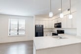Located at 100 Cabot Street in Boston, MA, this well-appointed one-bedroom, one-bathroom residence offers a thoughtfully designed layout that maximizes its compact footprint. The open-concept living and kitchen area serves as the heart of the home, featuring rich hardwood-style flooring that flows throughout the space. The kitchen is a standout, outfitted with crisp white cabinetry, light stone-finish countertops, a peninsula island with a built-in sink and pendant lighting overhead, and black appliances including a refrigerator, electric range, microwave, and dishwasher. Recessed lighting complements the natural light streaming in through the windows. The living area is open and airy, providing a versatile space adjacent to the kitchen. The bedroom offers a comfortable, well-proportioned retreat with a wall-mounted mini-split HVAC unit for individual climate control and direct access to a dedicated walk-in closet with wire shelving for organized storage. The full bathroom includes a clean, all-white tub and shower combination with chrome hardware. Consistent hardwood-style flooring and a neutral white color palette throughout lend the space a modern, cohesive aesthetic ideal for urban living in Boston.
