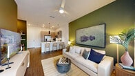 This one-bedroom, one-bathroom residence at Vistera in North Venice, Florida offers a thoughtfully designed open-concept layout across a single floor. The combined kitchen, dining, and living area serves as the heart of the home, featuring rich wood-tone cabinetry, white quartz countertops, a full suite of stainless steel appliances—including a French door refrigerator, range, microwave, and dishwasher—and a peninsula with bar seating illuminated by sleek pendant lighting. Wood-style flooring flows throughout the main living areas, grounding the space with warmth and continuity. The living room is distinguished by a bold deep-green accent wall, large windows with ample natural light, a ceiling fan, and access to a private patio through glass doors. The bedroom offers plush carpeting, multiple windows, and a ceiling fan, providing a calm and comfortable retreat. The walk-in closet includes built-in wire shelving and hanging systems for organized storage. The full bathroom features wood-tone cabinetry, a white undermount sink, and hardwood-style flooring, with open shelving nearby for linens. A dedicated laundry area completes the practical layout of this well-appointed North Venice residence.