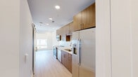 Located at 1408 Drexel Place in Charlotte, NC, this Strata Studio is a thoughtfully designed one-bedroom, one-bathroom residence that makes efficient use of its well-proportioned floor plan. Light hardwood-style flooring flows through the main living areas, while the bedroom features plush wall-to-wall carpet and a ceiling fan overhead.

The galley-style kitchen is a standout feature, showcasing warm wood cabinetry that extends to the ceiling, quartz countertops, a distinctive hexagonal white tile backsplash, and a full suite of stainless steel appliances including a flat-top range, over-the-range microwave, and refrigerator. Recessed lighting brightens the space throughout.

The bathroom is clean and contemporary, offering a wood-toned vanity with a quartz countertop, an illuminated mirror, and a glass-enclosed walk-in shower with chrome fixtures, all set against light hardwood flooring.

The bedroom is a comfortable retreat with soft carpeting, a ceiling fan, and direct access to the bathroom. The closet is outfitted with built-in shelving and hanging rods, and conveniently houses a stacked washer and dryer unit. Crisp white walls and a neutral palette throughout lend the space a bright, modern ambiance ideal for contemporary living.