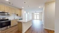 This well-designed single-floor residence offers a bright, open-concept layout with a seamless flow between the kitchen, dining, and living areas. The kitchen is a standout feature, equipped with light wood cabinetry extending to the ceiling, a full suite of stainless steel appliances including a French door refrigerator, electric range, microwave, and dishwasher. A large central island with a granite countertop provides ample prep and seating space, complemented by elegant pendant lighting and a classic subway tile backsplash. Warm hardwood-style flooring runs throughout the main living areas, enhancing the home's modern aesthetic. The spacious living room is bathed in natural light through large French doors topped with transom windows, and features a ceiling fan for added comfort. The bedrooms are carpeted and generously sized, each with ceiling fans and large windows that fill the rooms with natural light. The two bathrooms mirror the home's consistent design language, featuring wood-toned vanities with granite countertops, tiled tub-shower combinations, and walk-in closets. One bathroom includes a glass-enclosed walk-in shower. Throughout the space, neutral tones, clean lines, and quality finishes create a cohesive and inviting atmosphere.
