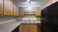 Located at 1175 Mathis Ferry Rd in the desirable Mt. Pleasant, South Carolina community, this single-floor residence offers a well-organized and practical layout. The kitchen is a standout feature, showcasing rich warm-toned wood cabinetry that extends to the ceiling, providing generous storage throughout. The cabinetry is complemented by stone-look countertops that wrap around the space in an L-shaped configuration, offering ample prep surface area. A double-basin stainless steel sink sits centered beneath upper cabinets, making cleanup and meal preparation convenient. Black appliances, including a refrigerator and range, add a cohesive, classic contrast to the wood tones. Overhead lighting illuminates the workspace effectively. The kitchen's design reflects a thoughtful use of space, with a layout that balances functionality and comfort. The neutral wall tones and consistent material choices throughout the kitchen contribute to a clean, inviting ambiance. Mt. Pleasant is known for its proximity to beaches, dining, and top-rated schools, making this an ideally situated property for those seeking both convenience and quality of life in the greater Charleston area.