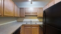 Located at 1175 Mathis Ferry Rd in the desirable Mt. Pleasant, South Carolina community, this single-floor residence offers a well-organized and practical layout. The kitchen is a standout feature, showcasing rich warm-toned wood cabinetry that extends to the ceiling, providing generous storage throughout. The cabinetry is complemented by stone-look countertops that wrap around the space in an L-shaped configuration, offering ample prep surface area. A double-basin stainless steel sink sits centered beneath upper cabinets, making cleanup and meal preparation convenient. Black appliances, including a refrigerator and range, add a cohesive, classic contrast to the wood tones. Overhead lighting illuminates the workspace effectively. The kitchen's design reflects a thoughtful use of space, with a layout that balances functionality and comfort. The neutral wall tones and consistent material choices throughout the kitchen contribute to a clean, inviting ambiance. Mt. Pleasant is known for its proximity to beaches, dining, and top-rated schools, making this an ideally situated property for those seeking both convenience and quality of life in the greater Charleston area.