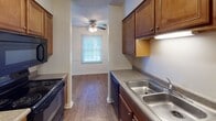 This single-floor unit at 604 W Colonial Dr in New Castle, Indiana, offers a straightforward and functional layout across several well-defined spaces. The floor plan, visible in the 3D model, reveals multiple rooms arranged for efficient use of space, with clear separation between living, sleeping, and utility areas.

The carpeted living area features a large sliding glass door fitted with vertical blinds, allowing natural light to filter in while providing a view to the outdoors. The textured ceilings are consistent throughout the carpeted rooms, lending a uniform aesthetic across the space.

The kitchen is equipped with rich, warm-toned wood cabinetry, dark countertops, a double stainless steel sink, and black appliances including a range and dishwasher. Wood-look flooring runs through the kitchen and connects to an adjacent dining or secondary living area, which features a ceiling fan and a window with blinds.

Multiple carpeted bedrooms offer neutral walls, textured ceilings, and windows that bring in natural light. One bedroom includes a closet with double doors. The unit includes two bathrooms: one featuring a tiled tub-shower combination with a granite-topped vanity, and a second with a walk-in shower enclosed by sliding glass doors, also paired with a wood-toned vanity and hardwood-style flooring.