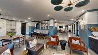 Located at 200 Walton Way Rd in Villa Rica, Georgia, this well-appointed single-floor amenity space offers a thoughtfully designed environment for socializing, relaxing, and staying active. The entrance welcomes visitors with polished concrete flooring, teal-accented trim, and clean white walls that establish the space's modern aesthetic throughout.

The expansive living room serves as the heart of the facility, showcasing bold blue-and-white patterned wallpaper, a wall-mounted flat-screen TV, and built-in navy cabinetry with a white countertop. Warm cognac leather chairs and a circular coffee table create an inviting seating arrangement, while large black-framed windows flood the room with natural light and offer views of the surrounding greenery.

The social dining area features a mix of booth-style banquette seating, round café tables, and a long communal bar-height table, all set against the same polished concrete floors and teal architectural accents. A fully equipped kitchen with stainless steel appliances completes this gathering zone.

The dedicated fitness room is bright and functional, with light wood-tone flooring, floor-to-ceiling mirrors, and large windows overlooking the outdoors. It is outfitted with cardio machines including treadmills, ellipticals, and stationary bikes, along with a dumbbell rack and storage for accessories. Ceiling fans ensure comfort during workouts.
