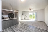 This two-story home is thoughtfully designed with a practical, neutral aesthetic throughout. The main level features an open-concept layout where the kitchen flows seamlessly into the living area. The kitchen is equipped with light wood cabinetry, a peninsula with a built-in sink, laminate countertops, and black appliances including a refrigerator, range, and over-the-range microwave. Durable wood-look vinyl plank flooring runs throughout the main level. The living area is bright and welcoming, highlighted by a ceiling fan, a large sliding glass door that opens to outdoor greenery, and a carpeted area that defines the lounge space. A staircase with a metal handrail connects to the upper level. A half bathroom on the main floor includes a dark-cabinetry vanity with a marble-style countertop and wood-look flooring. Upstairs, carpeted bedrooms offer comfortable, quiet retreats, each with windows that bring in natural light. A full bathroom features a tub-shower combination and coordinating dark vanity cabinetry. A spacious walk-in closet with wire shelving provides generous storage. Textured ceilings are present throughout the home.