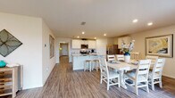 This single-story home offers a thoughtfully designed layout encompassing four bedrooms and two full bathrooms. The open-concept kitchen, dining, and living areas form the heart of the home, connected by warm wood-look luxury vinyl plank flooring that flows throughout the main spaces. The kitchen features white shaker-style cabinetry, granite countertops, a central island with bar seating, and a full suite of stainless steel appliances, including a range, microwave, and French door refrigerator. Recessed lighting illuminates the space efficiently. The adjacent dining area accommodates a full-size table and benefits from a door providing access to the exterior. The living room is bright and welcoming, with large windows that bring in natural light and offer outdoor views, complemented by recessed lighting overhead. The bedrooms carry a coastal design theme, with wood-look flooring and windows providing natural light. The bathrooms are finished with wood-look flooring and include a tub-shower combination. Throughout the home, a cohesive nautical and beach-inspired aesthetic ties the spaces together, creating a warm and inviting atmosphere.