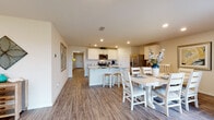 This single-story home offers a thoughtfully designed layout encompassing four bedrooms and two full bathrooms. The open-concept kitchen, dining, and living areas form the heart of the home, connected by warm wood-look luxury vinyl plank flooring that flows throughout the main spaces. The kitchen features white shaker-style cabinetry, granite countertops, a central island with bar seating, and a full suite of stainless steel appliances, including a range, microwave, and French door refrigerator. Recessed lighting illuminates the space efficiently. The adjacent dining area accommodates a full-size table and benefits from a door providing access to the exterior. The living room is bright and welcoming, with large windows that bring in natural light and offer outdoor views, complemented by recessed lighting overhead. The bedrooms carry a coastal design theme, with wood-look flooring and windows providing natural light. The bathrooms are finished with wood-look flooring and include a tub-shower combination. Throughout the home, a cohesive nautical and beach-inspired aesthetic ties the spaces together, creating a warm and inviting atmosphere.