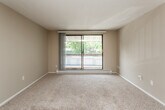 This single-floor residence offers a well-organized layout designed for comfortable everyday living. The living room serves as the central gathering space, finished with neutral-toned wall-to-wall carpeting and warm beige walls beneath a textured ceiling. A large sliding glass door dominates one wall, providing direct access to a private balcony and framing views of mature trees beyond. Baseboard heating runs along the perimeter, ensuring efficient climate control throughout the space.

The galley-style kitchen is efficiently arranged, featuring warm wood cabinetry lining both sides, dark laminate countertops, a stainless steel sink, and hardwood-style flooring. Black appliances, including a refrigerator and range, complete the functional setup.

The bedrooms are carpeted and bright, each receiving natural light through windows fitted with horizontal blinds that overlook surrounding greenery. One bedroom includes a closet with bifold doors, while a dedicated entry door provides a clear separation between the sleeping and living areas.

The bathroom is neatly appointed with a wood-framed medicine cabinet mirror, a single-sink vanity with wood cabinetry, and a full tub-shower combination. Hardwood-style flooring adds a warm contrast to the neutral walls, creating a clean, cohesive finish throughout the unit.