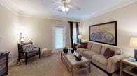 Located at 325 Spears Creek Church Rd in Columbia, SC, this single-floor residence offers a thoughtfully designed layout with a comfortable and cohesive interior throughout. The living room serves as the central gathering space, featuring crown molding, plush carpeting, a ceiling fan with light fixture, and multiple windows dressed with decorative curtains that allow for natural light. The kitchen is equipped with warm honey-toned cabinetry, dark granite-style countertops, tile flooring, and black appliances including a full-size refrigerator. Adjacent to the kitchen, the dining area provides a cozy setting accented by crown molding and a louvered closet door for added storage. The bedrooms are carpeted and well-sized, each offering ample natural light from large windows. One bedroom features a spacious walk-in closet with built-in wire shelving and hanging rods for generous storage capacity. The bathrooms include warm wood-toned vanities with dark countertops and tile flooring. One bathroom features a single vanity and toilet, while the second includes a full bathtub with a curtained surround. Overall, the space presents a warm, neutral palette with consistent finishes throughout.