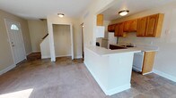 This multi-floor residence offers a practical and functional layout spread across three levels. The main floor features an open-concept living and dining area with a combination of tile and carpet flooring. Natural light enters through windows and a sliding glass door that leads to a small outdoor patio area, providing views of the surrounding community. A ceiling fan adds comfort to the living space. The kitchen is galley-style, equipped with warm wood cabinetry, white appliances including a refrigerator, electric range, and dishwasher, along with light countertops and a single-basin sink. A convenient half bathroom is also located on the main level. A coat closet near the entry adds practical storage. The upper floor houses two carpeted bedrooms, each benefiting from natural light through multiple windows. Two full bathrooms serve the upper level, each finished with simple, clean fixtures. The lower level contains an unfinished basement with painted concrete floors, exposed ceiling joists, and in-unit laundry hookups with a washer already in place, offering additional storage potential. Central air conditioning services the home.