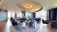 Located at 30 Peabody Street in Nashville, TN, this elegantly appointed high-rise lounge offers a generously proportioned single-floor layout with an expansive open-plan interior and a dedicated outdoor balcony. Floor-to-ceiling glass walls wrap the perimeter, flooding the space with abundant natural light and framing sweeping panoramic views of the Nashville skyline and surrounding cityscape.

The interior design is defined by a sophisticated contemporary aesthetic. A signature curved tray ceiling serves as an architectural focal point, adorned with sculptural globe chandeliers that cast warm ambient light throughout the lounge. The open seating area is thoughtfully arranged with plush velvet curved sofas, club chairs, and intimate conversation groupings positioned atop large area rugs over warm hardwood flooring. Textured stone-clad columns add visual depth and structural character throughout.

A full bar area features custom teal cabinetry with glass-front displays, pendant lighting, bar seating, and a built-in beverage cooler — ideal for social and hospitality functions. The space transitions seamlessly to an expansive outdoor balcony, finished with large-format tile, lush planters, and multiple seating arrangements that capture unobstructed views of the downtown Nashville skyline, making it a standout feature of the overall experience.