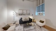 Located on Prospect Avenue in Cleveland, OH, this one-bedroom, one-bathroom unit offers a thoughtfully designed layout across a single floor. The open-concept living, dining, and kitchen area serves as the heart of the home, highlighted by dramatically soaring ceilings with exposed industrial ductwork and concrete columns that lend a distinctive loft-like character. Large windows allow natural light to fill the living space, which features warm hardwood-style flooring throughout.

The kitchen is outfitted with light wood cabinetry, stainless steel appliances including a range, microwave, dishwasher, and refrigerator, complemented by a bold geometric tile backsplash and a breakfast bar with seating. A hallway lined with clean white walls and louvered closet doors connects the main living area to the private quarters.

The bedroom is a serene retreat with plush carpet, a wall-mounted mini-split system for climate control, and easy access to in-unit laundry. The full bathroom features hexagonal tile flooring, a glass-enclosed shower, a light wood vanity with white countertops, and matte black fixtures for a contemporary finish. A dedicated closet, utility room, and entrance complete this efficiently organized and modern urban residence.