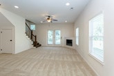 This two-story home is designed with an open and functional layout across both levels. The main floor centers around a large living area finished with plush carpet, a ceiling fan, and abundant natural light streaming through multiple windows. A corner fireplace with French doors nearby adds warmth and character to the space, while recessed lighting provides consistent illumination throughout.

The kitchen is well-appointed with warm-toned wood cabinetry, dark countertops, stainless steel appliances including a refrigerator and microwave, and a central island with pendant lighting overhead. Hardwood-style flooring runs through the kitchen, complementing the carpet in the adjoining living areas. A front entryway with a view corridor connects the main spaces efficiently.

The upper level features carpeted bedrooms, each with ample closet space including a sizable reach-in closet with wire shelving. A hallway connects the rooms and leads to multiple bathrooms. The bathrooms include wood-toned vanities with white countertops, large mirrors, and tub-shower combinations set on tile flooring. A staircase with a classic baluster railing links the two floors, as seen in the 3D layout view.