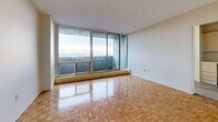 This efficiently designed single-floor unit offers a practical layout comprising a living room, kitchen, hallway, and full bathroom. The living room is the standout space, featuring classic parquet wood flooring in a herringbone-style pattern and a full-width floor-to-ceiling window that frames sweeping panoramic views, filling the room with abundant natural light. The open sightlines create an airy, expansive feel well beyond the unit's compact footprint. The kitchen is neatly arranged with light wood cabinetry, a white electric range, refrigerator, and a sink, all set on smooth hardwood-style flooring that contrasts warmly with the cabinetry. A large sliding-panel closet in the hallway provides generous built-in storage, while the hallway itself connects all areas of the unit seamlessly. The bathroom is cleanly appointed with white tile flooring, a tub-shower combination surrounded by pastel-toned square wall tiles, a toilet, and a vanity with a white countertop and modern hardware. Throughout the unit, neutral cream-toned walls maintain a bright, clean aesthetic that complements the warm wood flooring found in the main living areas. The overall ambiance is practical and understated, with the expansive view serving as the defining architectural highlight.