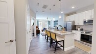 This single-floor, one-bedroom, one-bathroom unit in Greenwood, Indiana offers a thoughtfully organized layout that maximizes its compact footprint. Light-toned wood-style flooring runs throughout the main living areas, creating a cohesive and contemporary aesthetic.

The kitchen is a standout feature, equipped with white shaker-style cabinetry, a gray tile backsplash, stainless steel appliances, and a large center island with a built-in sink and seating for multiple bar stools illuminated by pendant lighting. The kitchen flows seamlessly into the living room, which features large windows that invite natural light and provide exterior views. A ceiling fan, neutral walls, and a private balcony accessible via a glass-paneled door complete the space.

The bedroom offers large windows overlooking the exterior, a double-door closet, and neutral carpet. The bathroom includes a white vanity with a gray quartz-style countertop, an undermount sink, and wood-style flooring. Throughout, clean white trim and doors contribute to the unit's modern, well-finished character.