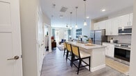 This single-floor, one-bedroom, one-bathroom unit in Greenwood, Indiana offers a thoughtfully organized layout that maximizes its compact footprint. Light-toned wood-style flooring runs throughout the main living areas, creating a cohesive and contemporary aesthetic.

The kitchen is a standout feature, equipped with white shaker-style cabinetry, a gray tile backsplash, stainless steel appliances, and a large center island with a built-in sink and seating for multiple bar stools illuminated by pendant lighting. The kitchen flows seamlessly into the living room, which features large windows that invite natural light and provide exterior views. A ceiling fan, neutral walls, and a private balcony accessible via a glass-paneled door complete the space.

The bedroom offers large windows overlooking the exterior, a double-door closet, and neutral carpet. The bathroom includes a white vanity with a gray quartz-style countertop, an undermount sink, and wood-style flooring. Throughout, clean white trim and doors contribute to the unit's modern, well-finished character.