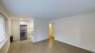 Located at 1001 Sherman Street in Denver, Colorado, this single-floor unit offers a straightforward and functional layout designed for comfortable everyday living. The open living area is finished with warm hardwood-style flooring that runs throughout, complemented by crisp white walls and smooth ceilings that create a bright, airy atmosphere. The kitchen is positioned adjacent to the living space and features stainless steel appliances, including a full-size refrigerator, white cabinetry, and a small breakfast bar with bar seating — ideal for casual dining. A half-wall partition neatly defines the kitchen area while maintaining an open connection to the main living space. A doorway from the living area leads to additional rooms beyond, suggesting a practical and well-connected floor plan. The overall aesthetic is clean and minimal, with a neutral palette that provides a versatile backdrop for a variety of interior styles. The unit's single-floor design ensures easy accessibility and a cohesive flow from room to room. Situated in Denver's Capitol Hill neighborhood, the property is well-positioned near local amenities, parks, and city conveniences.