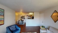 This single-story residence is designed with a functional, open-concept layout that connects the main living areas seamlessly. The living room is a comfortable, well-lit space featuring dark hardwood-style flooring, a textured ceiling, and a large sliding glass door fitted with vertical blinds that allows natural light to flow in while providing views of the surrounding greenery outside.

Adjacent to the living room, the dining area accommodates a round table beneath a pendant light fixture, with the kitchen positioned just beyond a half-wall pass-through. The kitchen is equipped with warm wood cabinetry, granite-style countertops, black appliances including a gas range and refrigerator, and a flush-mount ceiling light.

The two bedrooms feature carpeted floors, reach-in closets, and textured ceilings. One bedroom includes a built-in shelving unit within the closet. Both bathrooms are finished with hardwood-style flooring, vanities with granite-style countertops, and shower-tub combinations with curtain rods. The neutral color palette and consistent finishes throughout contribute to a cohesive and practical living environment.