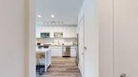 Located at 300 Atlas St in Baltimore's vibrant 21230 zip code, this single-floor residence offers a thoughtfully designed layout with contemporary finishes and an abundance of natural light throughout. The kitchen is a standout feature, showcasing high-gloss white cabinetry extending to the ceiling, a classic subway tile backsplash, stone countertops, and a full suite of stainless steel appliances including a range, built-in microwave, dishwasher, and refrigerator. A central island with seating adds both functionality and style, while light wood-tone flooring ties the space together seamlessly. The open living area is bright and airy, anchored by large floor-to-ceiling windows and a glass-paned door that invites natural light and offers views of the surrounding Baltimore streetscape. A ceiling fan adds comfort, and the neutral palette creates a welcoming, versatile atmosphere. The bedroom is generously proportioned, featuring wide windows with urban views, a ceiling fan, and wood flooring that carries throughout. The bathroom is clean and modern, with large-format tile flooring, a wood-toned vanity with white countertop, and a full tub-shower combination. An adjacent walk-in closet provides ample storage. Overall, this residence delivers a polished, contemporary living experience in the heart of Baltimore.